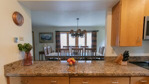 Una cucina con piani in granito, mobili in legno, un tavolo da pranzo con sedie, un lampadario e una ciotola di frutta.