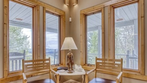 A corner room with two wooden chairs, a small table, a lamp, and large windows with a view of trees and a deck. - Berg Stuga, Free Attraction Tickets, Game Room, Hot Tub, WIFI!!! (Townsend)