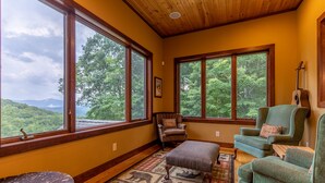 A cozy room with large windows, a wooden ceiling, and a view of the forest.