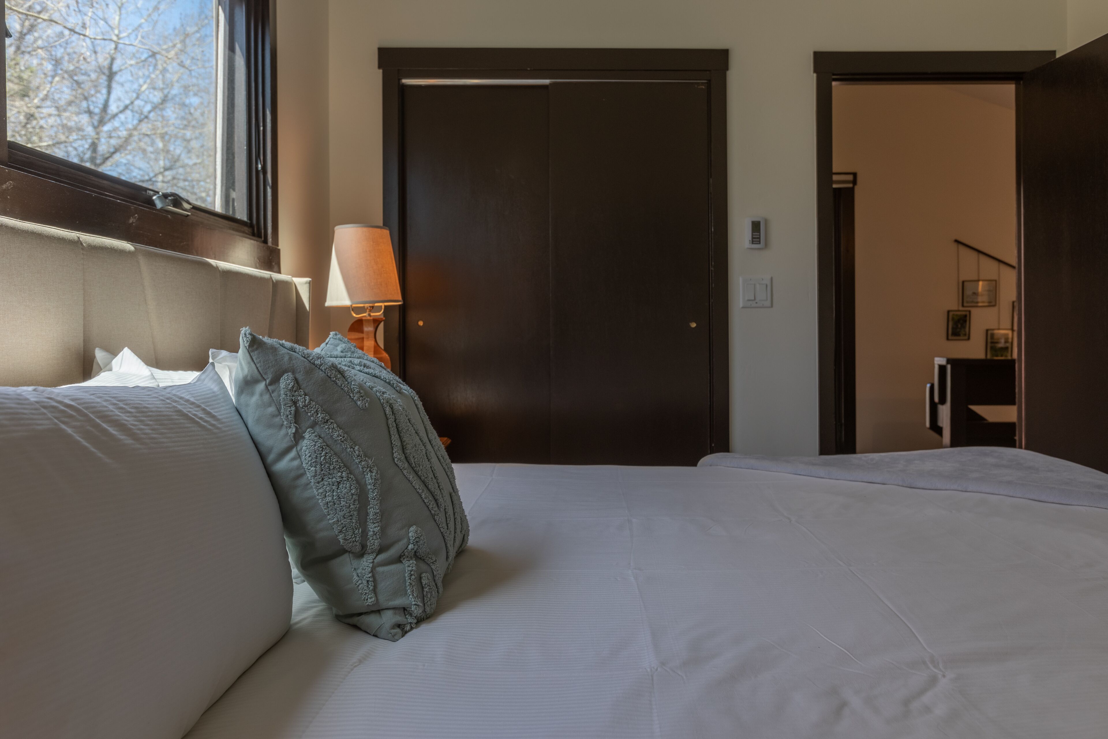 A bedroom with a large bed, a window, a door, and a lamp.