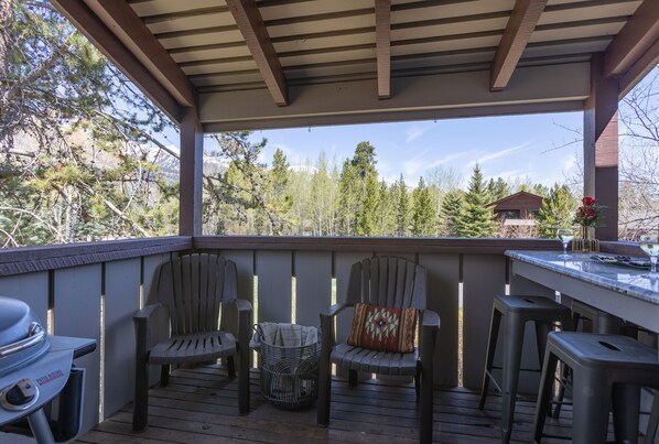 A covered outdoor deck with wooden chairs, a barbecue grill, and a bar area.