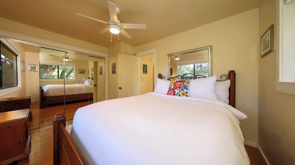 A bedroom with a large bed, a ceiling fan, a dresser, and a mirror.