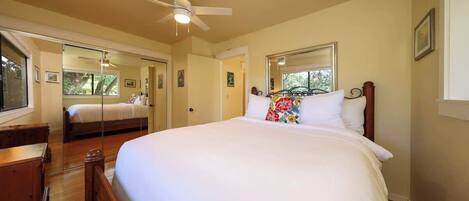 A bedroom with a large bed, a ceiling fan, a dresser, and a mirror.