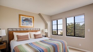 Une chambre avec un grand lit, deux tables de chevet avec des lampes, un tableau encadré au mur et une fenêtre donnant sur des arbres.
