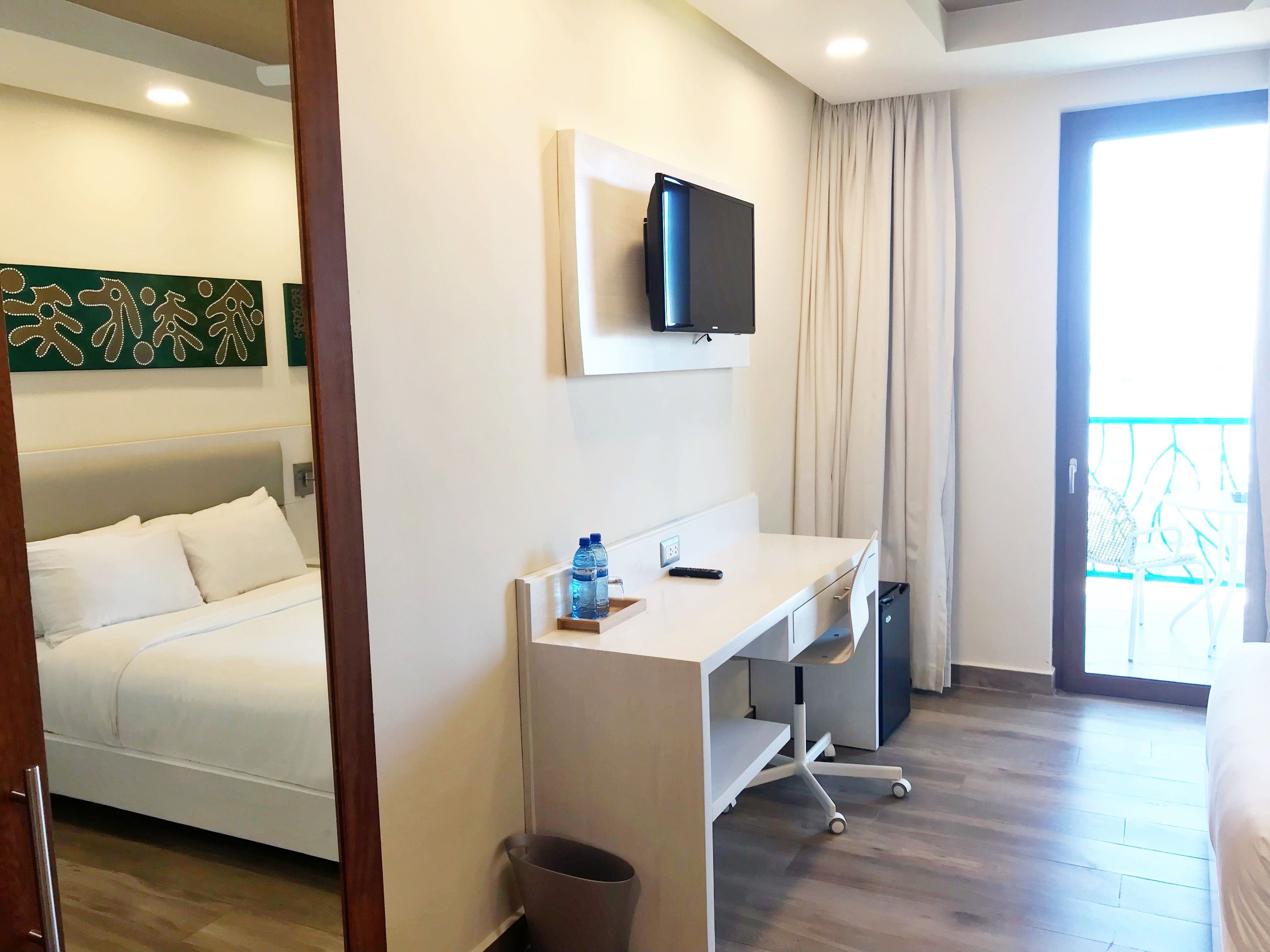 A hotel room with a bed, a desk, a TV, and a balcony.
