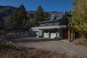 Una casa moderna de dos pisos con paneles solares en el techo, un muro de piedra y un camino de entrada que lleva al garaje.