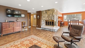 A spacious living room with a fireplace, wooden flooring, a flat-screen TV, and a dining area with a table and chairs. - Pets OK, OCEAN VIEW, Beach Path, HOT TUB, Large Yard (FirstM) (Ocean Park)