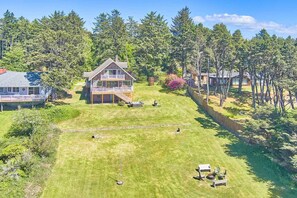 A two-story house with a deck, surrounded by a well-maintained lawn and dense forest. - Pets OK, OCEAN VIEW, Beach Path, HOT TUB, Large Yard (FirstM) (Ocean Park)