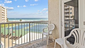 A balcony with a view of a tennis court and the ocean. There are two white chairs and a door with blinds. - 308- "Embrace Coastal Charm: Experience Beach Cottage Vibes in Destin" (Destin)