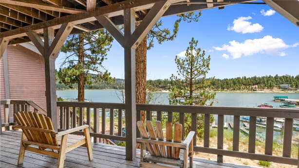 A wooden deck with two Adirondack chairs overlooking a lake with boats, surrounded by trees and a building. - LAKEFRONT - Boat Dock! Close to Slopes, HOT TUB! Game room! (Big Bear Lake)