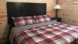 A bedroom with a wooden headboard, a plaid bedspread, and a 'farmhouse' sign on the wall.