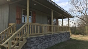 A two-story building with a stone foundation, wooden steps, and a covered porch with a railing.