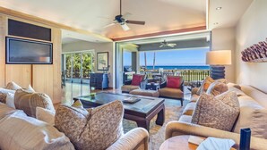 A spacious living area with a large sofa set, a coffee table, and a ceiling fan. There is a view of the ocean through large windows. - Hualalai Golf Villa 4202 - Oceanfront + Prime Location + Room Service (Kailua Kona)