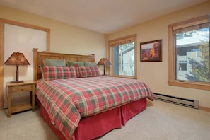 A bedroom with a plaid bedspread, two bedside lamps, a window with a view, and a framed picture on the wall.