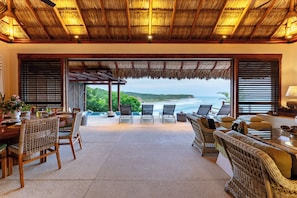 A spacious outdoor seating area with a view of the ocean, furnished with wicker chairs and a dining table. - Luxe Beach Villa in 5-star Oceanfront Community (Huatulco)