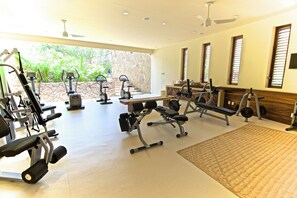 A gym with various exercise equipment, a stone wall, and large windows. - Luxe Beach Villa in 5-star Oceanfront Community (Huatulco)
