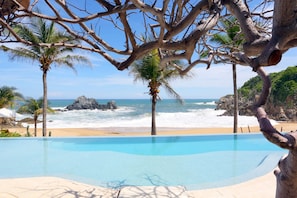 A clear blue pool with a view of the ocean and rocky coastline. - Luxe Beach Villa in 5-star Oceanfront Community (Huatulco)