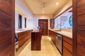 A modern kitchen with wooden cabinets, a central island, and a built-in dishwasher. - Luxe Beach Villa in 5-star Oceanfront Community (Huatulco)