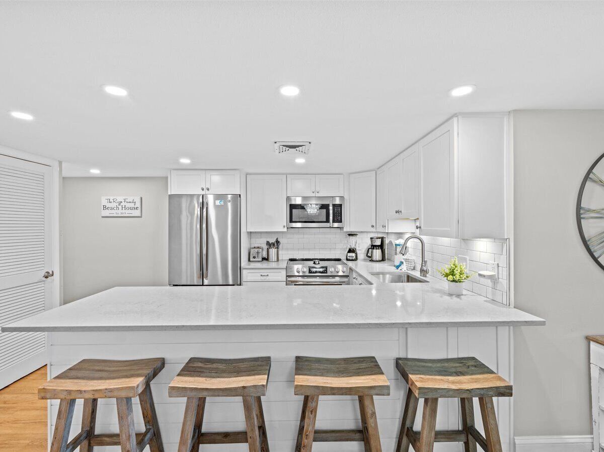 Cozinha moderna com armários brancos, eletrodomésticos de aço inoxidável e uma ilha central com banquetas.