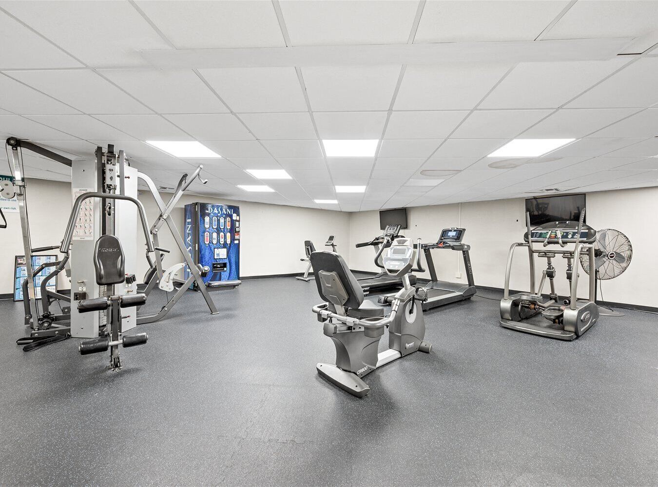 Une salle de sport équipée de divers appareils d’exercice, notamment un tapis de course, un vélo elliptique et des appareils de musculation.