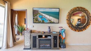 Un soggiorno con camino, un grande quadro incorniciato che raffigura un resort sulla spiaggia e uno specchio rotondo con decorazioni a foglia.