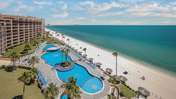 Un resort con diverse piscine, una spiaggia e un ampio edificio alberghiero.