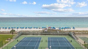 A tennis court with a view of the beach and ocean.