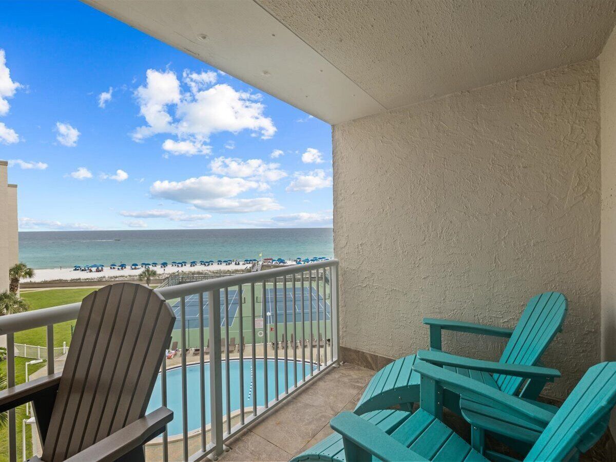 A balcony with a view of the beach and ocean. There are two Adirondack chairs and a pool.
