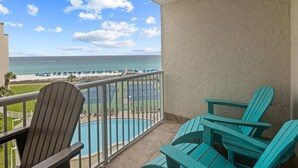 A balcony with a view of the beach and ocean. There are two Adirondack chairs and a pool.