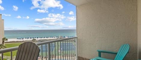 A balcony with a view of the beach and ocean. There are two Adirondack chairs and a pool.