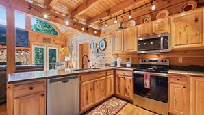 A wooden cabin-style kitchen with a large island, stainless steel appliances, and a rustic decor. - Charming 2 BR Log Home Super Views Paved Access Gravel Drive Hot Tub, & WIFI (Maggie Valley)