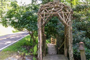 A rustic wooden archway leading to a wooden staircase surrounded by lush greenery.