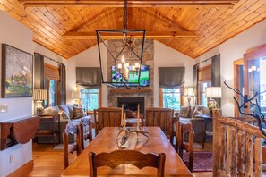 A spacious room with a wooden ceiling, a stone fireplace, and a dining table surrounded by chairs.