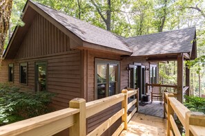 A wooden cabin with a porch, surrounded by trees.