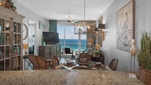 A spacious living room with a large window overlooking the ocean, a dining area with a granite countertop, and a cozy seating area with a fireplace. - 2306 - Nautical Style Couples Retreat (Panama City Beach)