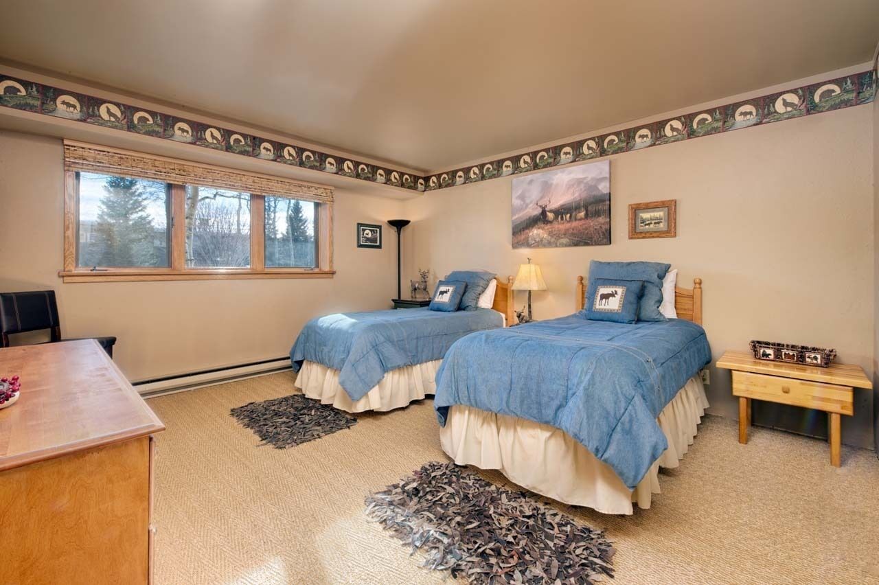 Una camera da letto con due letti, una scrivania in legno, una finestra con persiane e un quadro appeso al muro.
