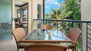 A balcony with wicker furniture, a glass table, and a view of palm trees and a clear sky. - F302 - Amazing Location! Modern, Clean Furnishings - Sleeps 6 in AC Comfort! (Kapaa)