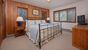 A bedroom with a wooden paneled wall, a bed with a metal frame, two bedside lamps, a television on a wooden cabinet, and a window with blinds. - JHRL - Teewinot D4, Great Slopeside Location (Teton Village)