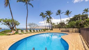 A swimming pool with a curved edge, surrounded by palm trees and lounge chairs. - Oceanfront Kihei Beach Unit 410 Panoramic Views  Steps to the Beach! (Kihei)
