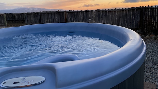 Un bain à remous doté d’un panneau de commande, entouré d’une clôture en bois et sous un ciel dégagé.