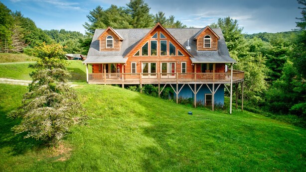 A log cabin with a covered porch and a deck, surrounded by lush greenery. - 1 Awesome Skyview - Spectacular log home with hot tub and  top of the line amenities! (Vilas)
