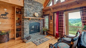 A cozy cabin interior with a stone fireplace, wooden shelves, and a balcony with a scenic view. - 1 Awesome Skyview - Spectacular log home with hot tub and  top of the line amenities! (Vilas)