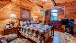 A cozy log cabin bedroom with a bed, two bedside tables, a dresser, a television, and a window with a view. - 1 Awesome Skyview - Spectacular log home with hot tub and  top of the line amenities! (Vilas)