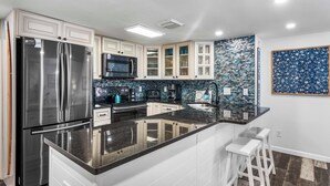 A modern kitchen with white cabinetry, a stainless steel refrigerator, a black microwave, and a tiled backsplash. - 121- Ground floor unit-steps to the wonderful beach, W/D in unit,FREE Bch Svc (Destin)