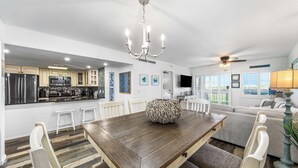 A modern kitchen with stainless steel appliances, a dining area with a wooden table and white chairs, and a living room with a sofa and a ceiling fan. - 121- Ground floor unit-steps to the wonderful beach, W/D in unit,FREE Bch Svc (Destin)