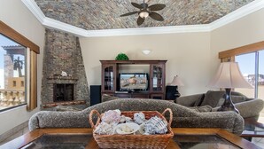 A living room with a stone fireplace, a television, a sofa, and a coffee table with a basket of seashells.