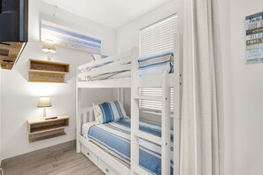 A bunk bed room with a TV, bedside lamp, and wooden shelves.