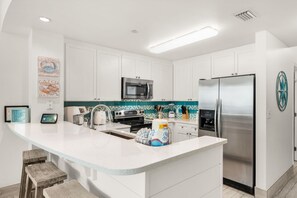 A modern kitchen with white cabinetry, a stainless steel refrigerator, a microwave, and a large island with bar stools.
