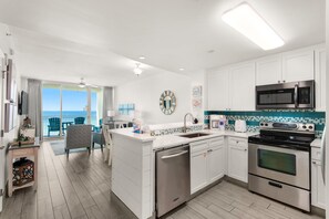A modern kitchen with white cabinetry, a stainless steel stove, and a microwave. There is a balcony with a view of the ocean.
