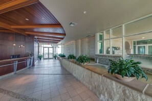 A spacious lobby with a wooden ceiling, a reception desk, and a seating area with potted plants.